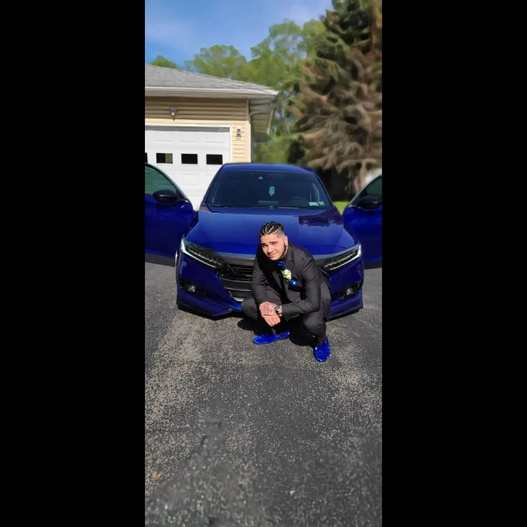 Client in black suit with blue crystal loafers posing with matching blue car
